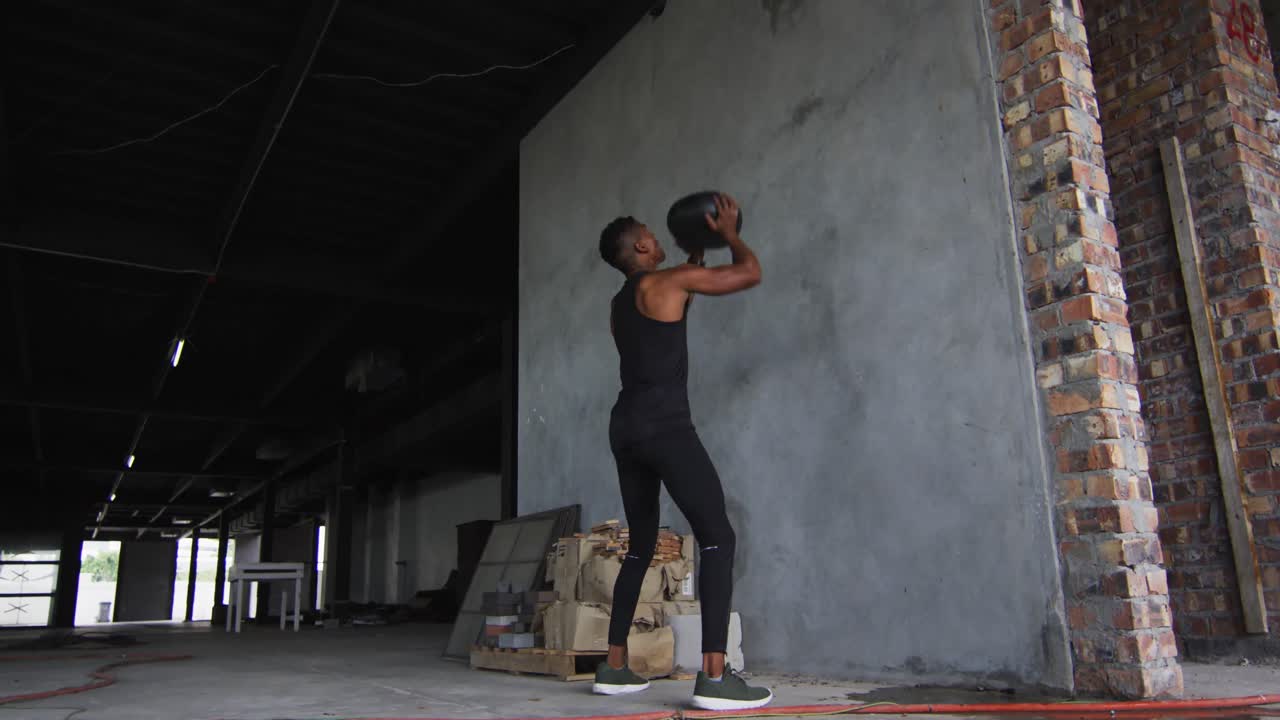 African american man exercising with medicine ball in an empty urban building