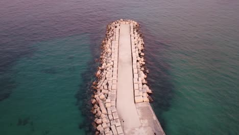 aerial view of stony jetty surrounded by crystal clear ocean water during sunset