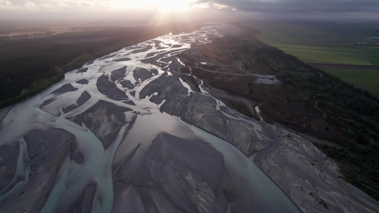 volando sobre el río trenzado waimakariri hacia la puesta de sol con rayos de luz en christchurch, nueva zelanda