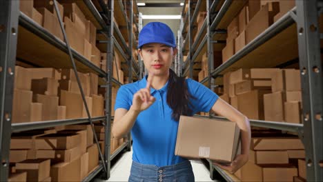 mensajera asiática en uniforme azul que no muestra ningún gesto mientras entrega un cartón en el almacén
