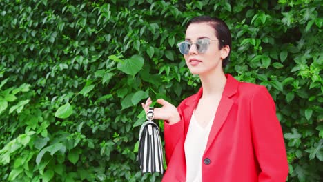 mujer elegante llevando una bolsa de pie frente al seto verde