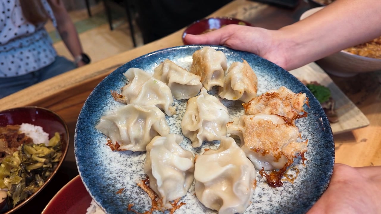 Close-up of hands holding a blue ceramic plate with gyoza and potstickers in Bangkok.