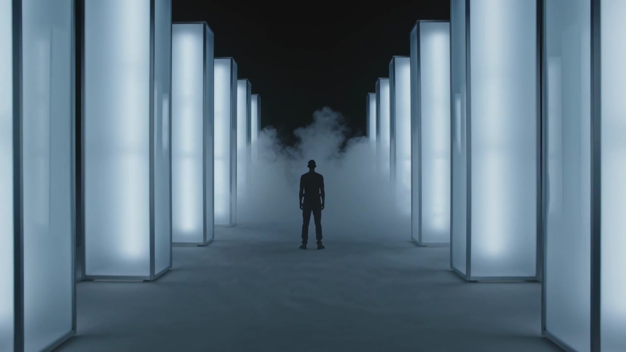 Standing man in dark outfit between lit columns while fog machine releasing fog, creating depth