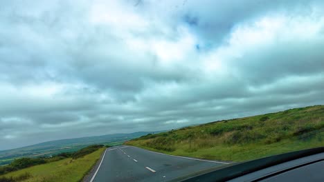tilted pov car dashcam angle driving along hill road with ominous clouds in sky as vehicle descends towards rural village in south wales in gower pensinsula. travel, transportation clip