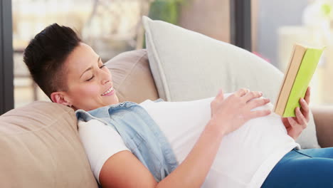 pregnant woman reading a book while lying on the couch