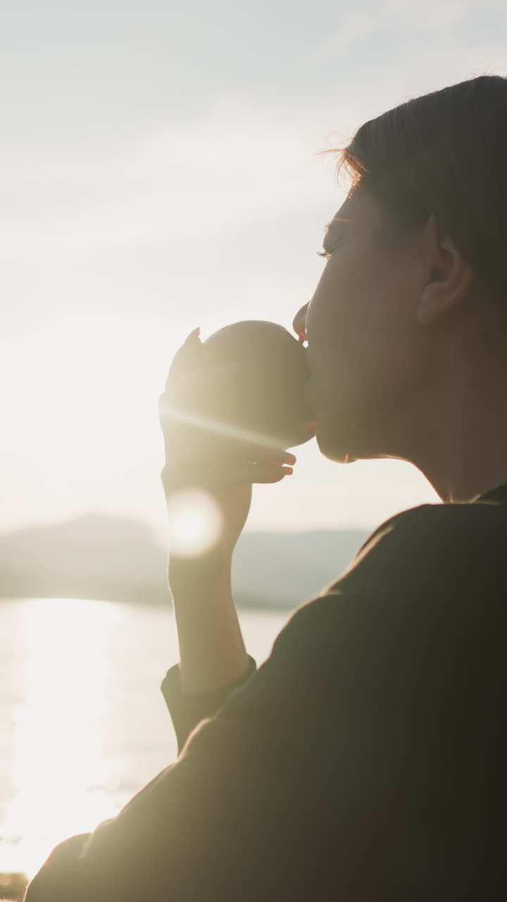 해가 지는 동안 호수 근처에서 사과를 먹는 여자, 외로운 여자가 산과 호수의 전망을 즐기며 과일을 먹는 여성, 은 가을 날, 주말 휴식