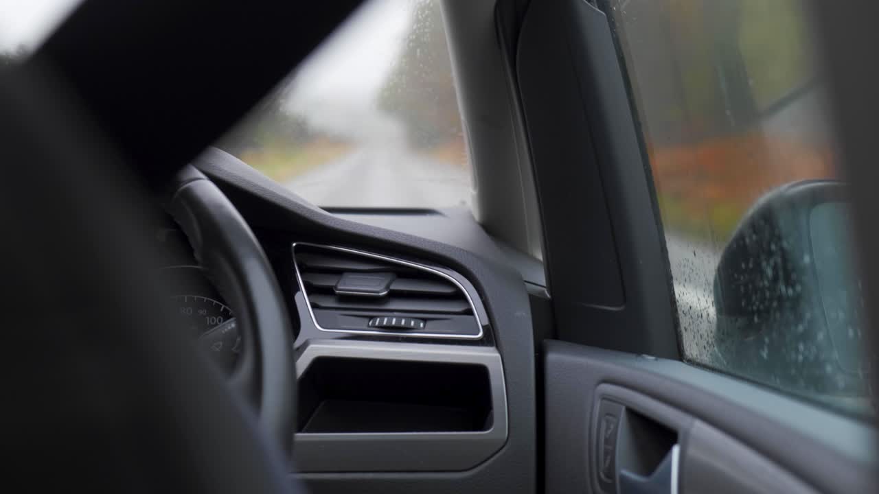Rainy day view from inside a car with a blurred road and water droplets on the window