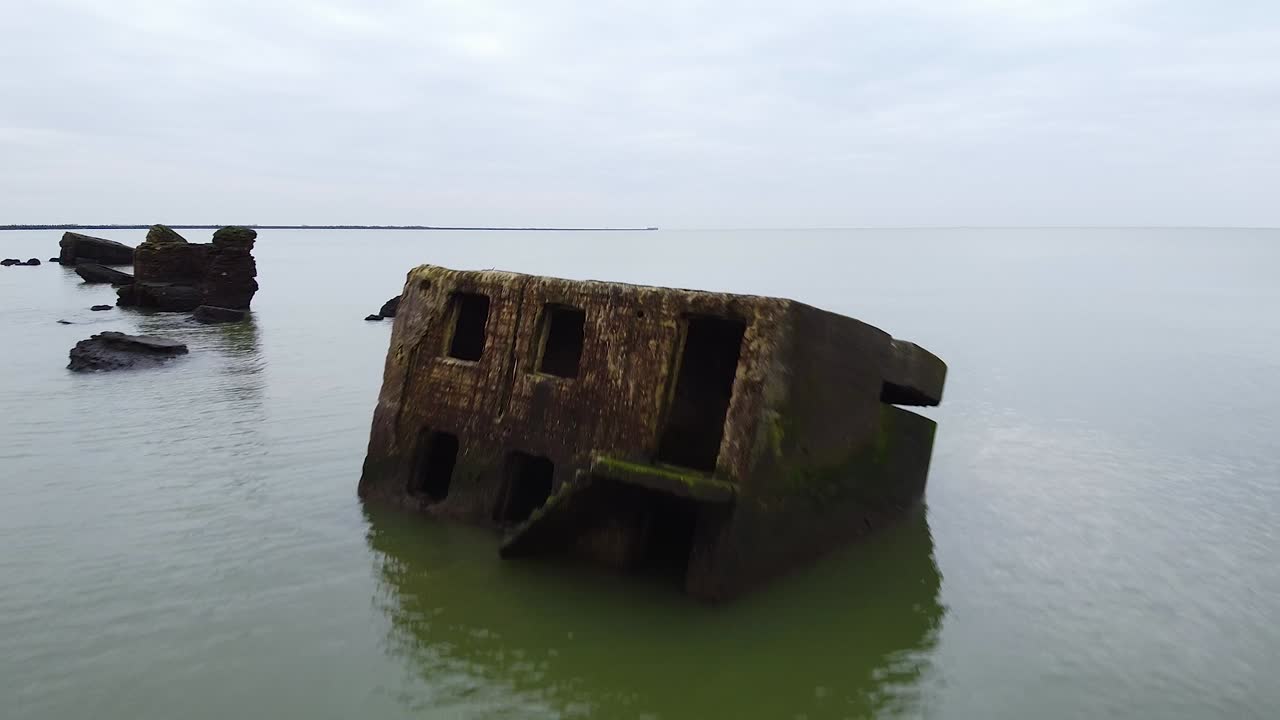 Aerial view of abandoned seaside fortification bunker in water at Karosta Northern Forts on the beach of Baltic sea in Liepaja in overcast spring day, descending revealing drone shot moving backwards
