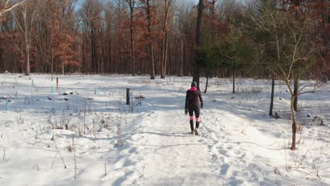 woman wearing warm exercise clothing walking alone on winter snowy forest path