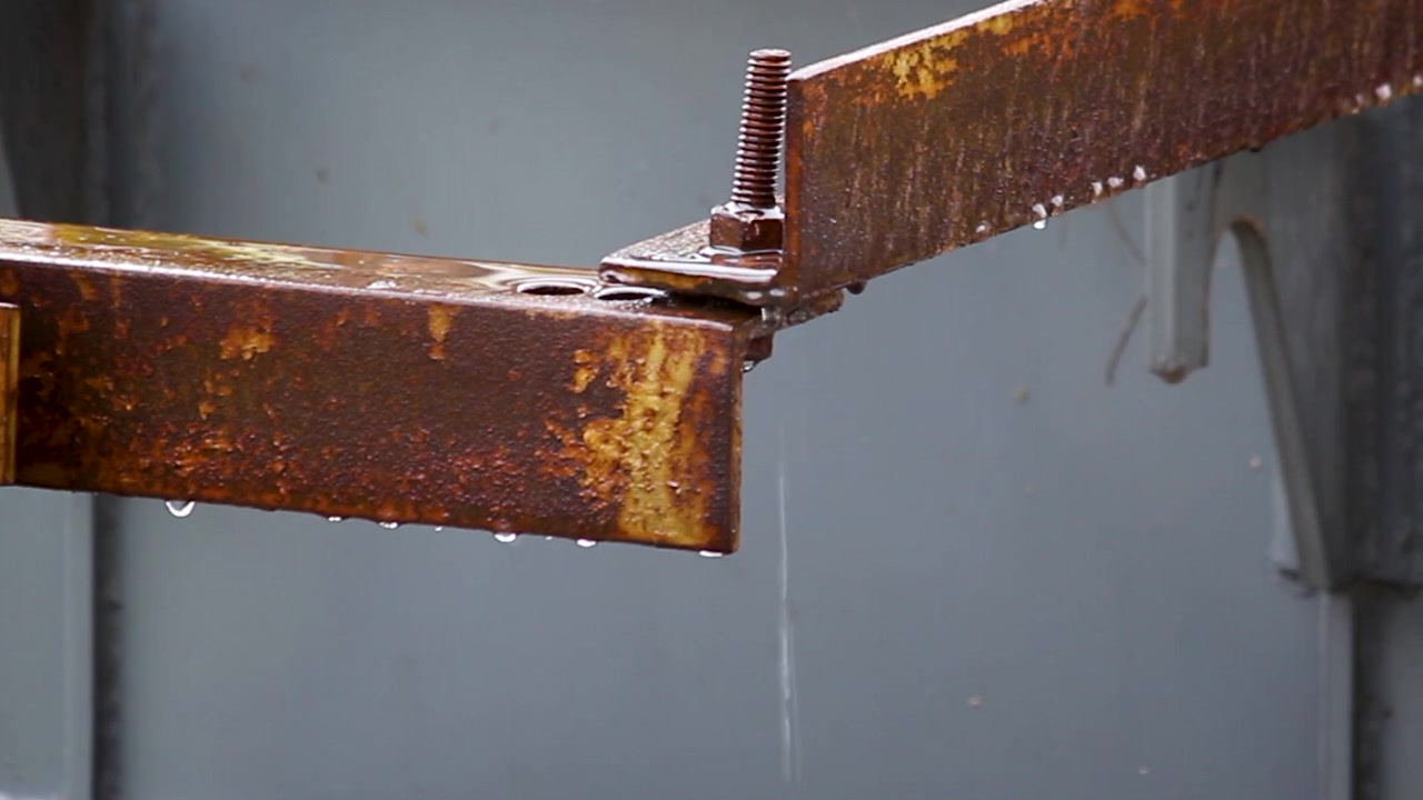 Close-up of rainwater dripping from a rusted steel beam connection. Ideal for construction, infrastructure maintenance, corrosion, weather, industrial safety, and engineering projects.