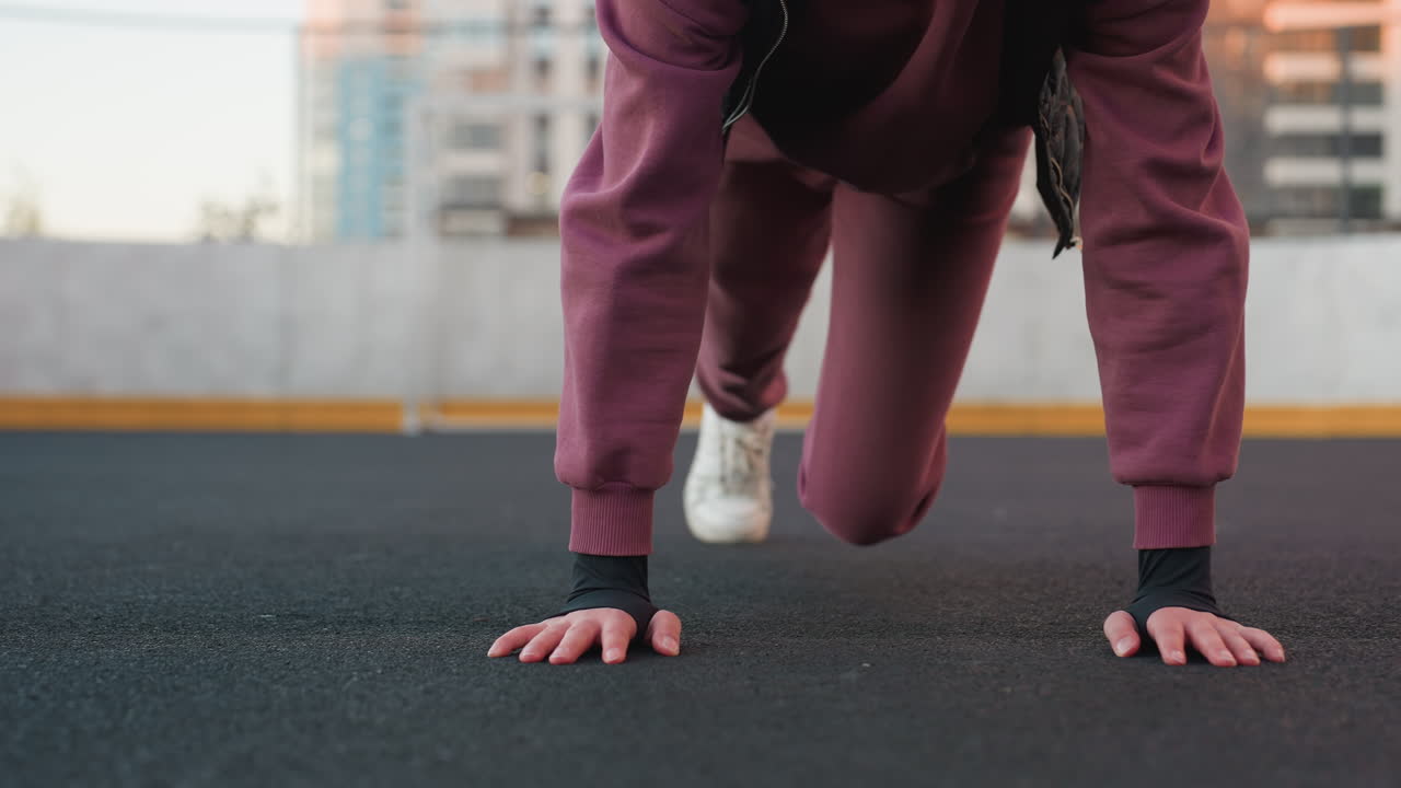 Hoodie wearing athlete doing foot crawl exercise on urban sports court floor with hands pressing ground and legs moving simultaneously for core stability strength mobility during outdoor city workout
