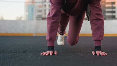 hoodie wearing athlete doing foot crawl exercise on urban sports court floor with hands pressing ground and legs moving simultaneously for core stability strength mobility during outdoor city workout