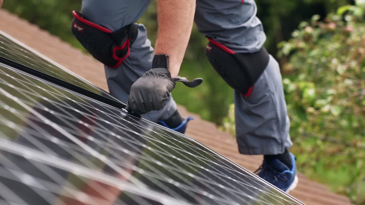 Mand reparerer solpanel på tag med knæbeskyttere på, statisk visning.