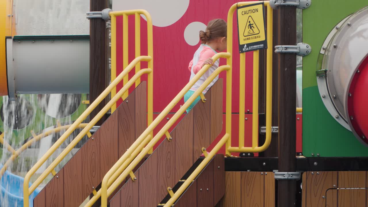 niña de tres años con coletas subiendo las escaleras para montar en tobogán en el parque acuático