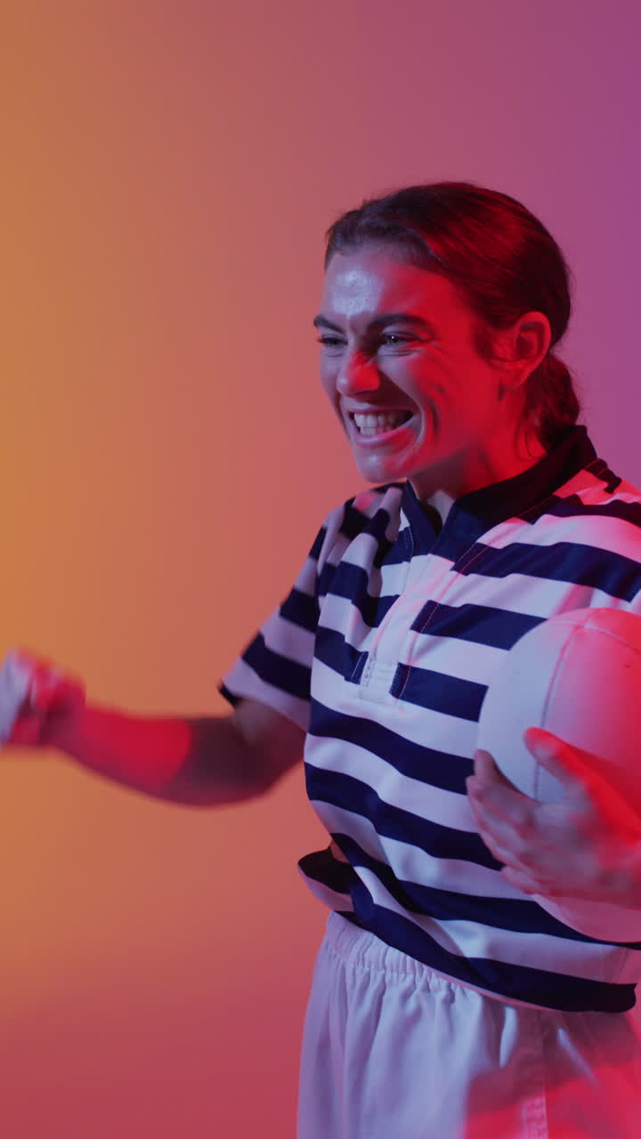 video vertical de una feliz jugadora de rugby caucásica levantando las manos sobre la iluminación rosa de neón