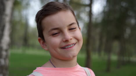 Portrait-of-cheerful-boy-in-brackets-outdoors.-Cute-guy-smiling-in-garden.