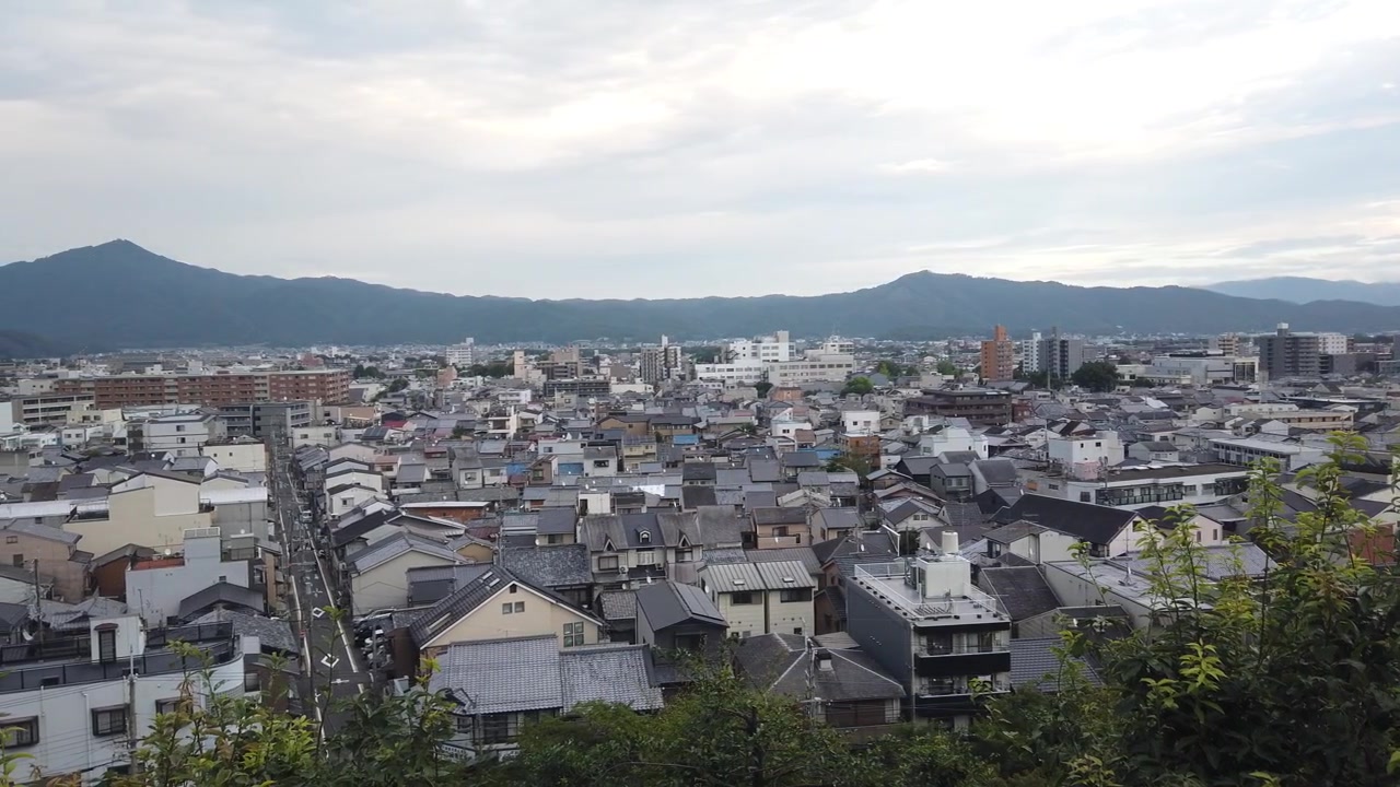 Vista aerea di un quartiere affollato nella città di Kyoto, capitale storica del Giappone, che mostra una zona residenziale giapponese con uno sfondo montuoso, strade asfaltate e tetti.