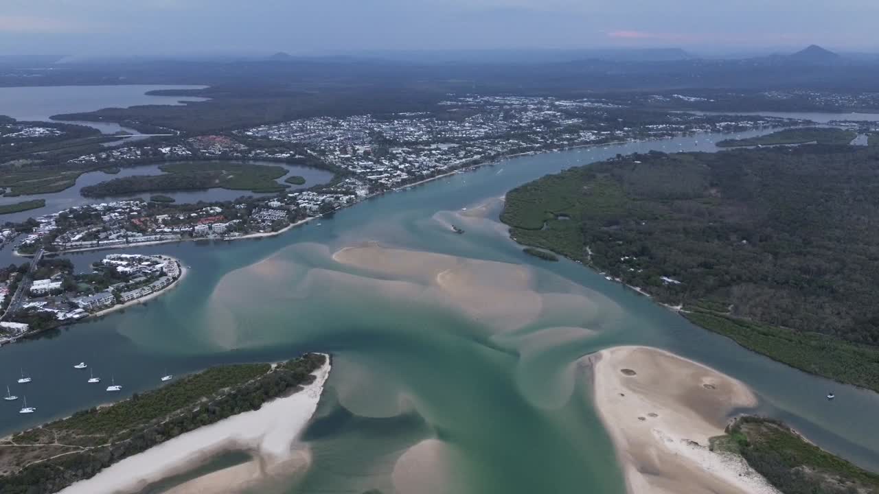 Drone footage reveals the coastal landscape of Noosa Spit and the town of Noosa in the distance. A smooth aerial reveal over the turquoise water captures the serene beauty of Queensland’s coastline.