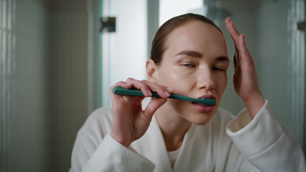 Young woman brushing teeth at home closeup. Pretty girl looking camera cleaning