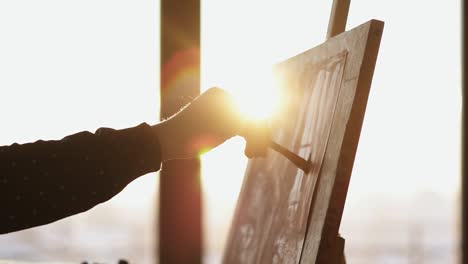 female hand drawing with paint on canvas that is placed on easel.