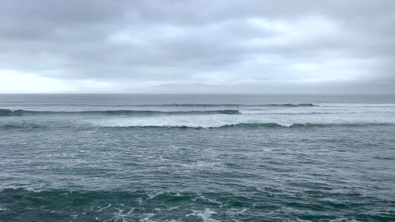 Slow-motion footage of waves crashing against the shore along the Portuguese coastline. Surfers glide across the water under a moody sky, capturing the dynamic and serene beauty of the sea.