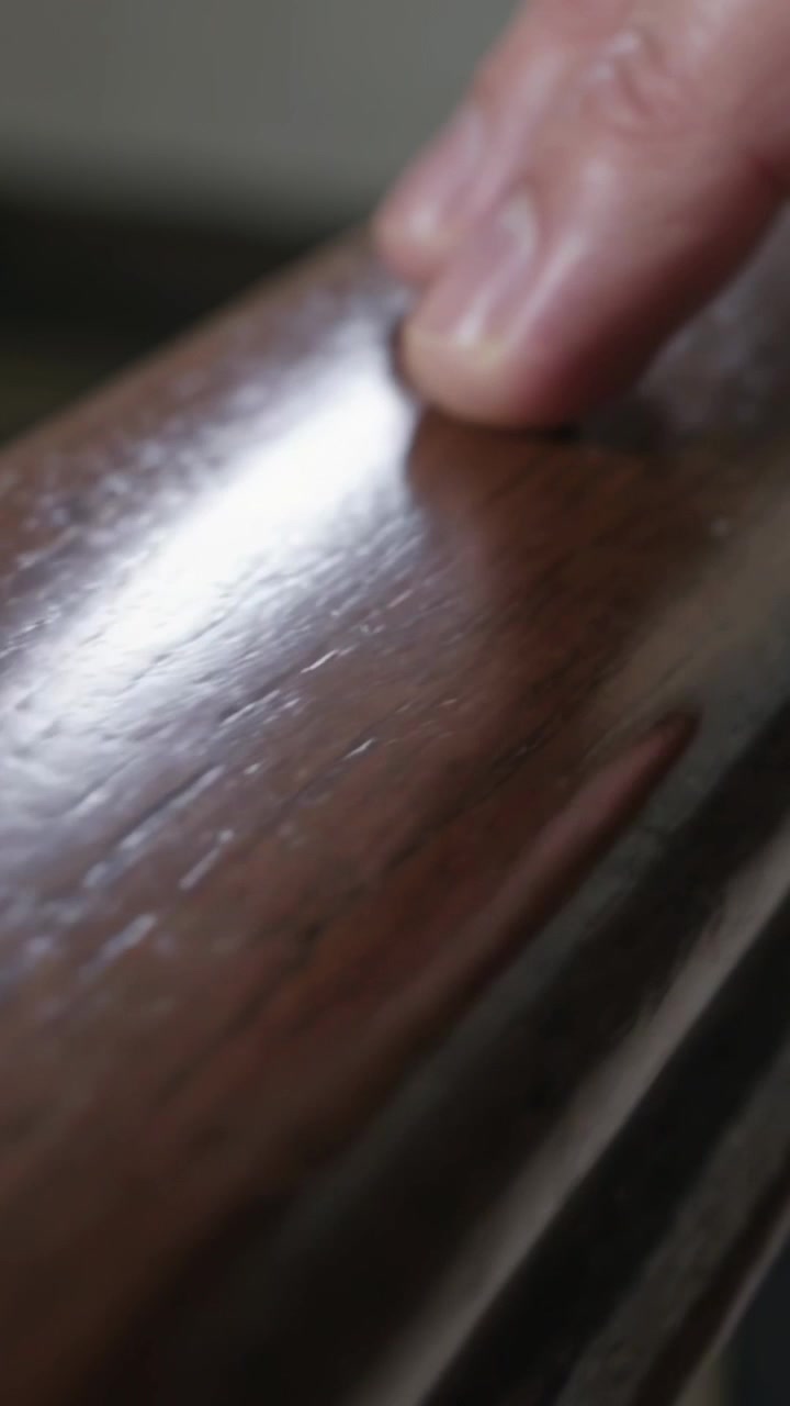 Vertical video: Gliding fingertip on first touch along wood rail checking finish on home stairs
