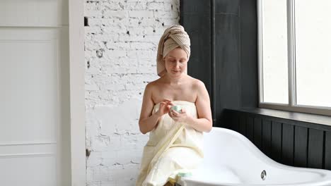 smiling woman in towel sitting on bathtub with cream