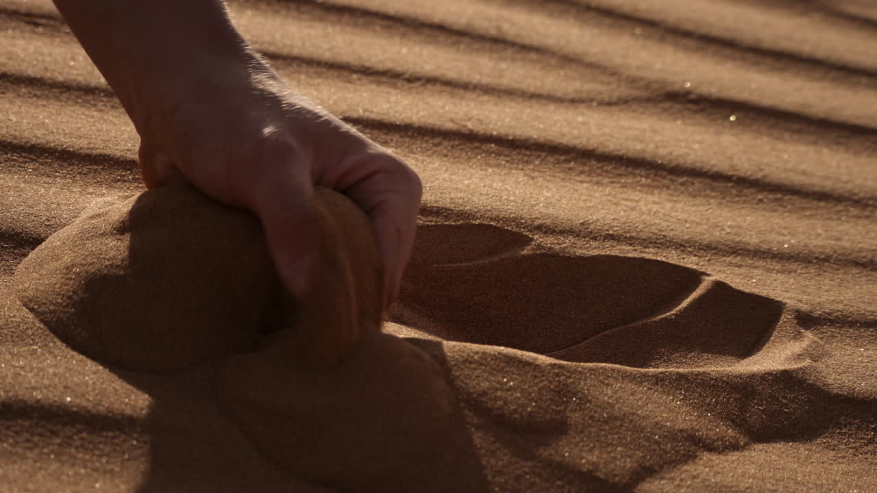 Hand pouring sand in the desert