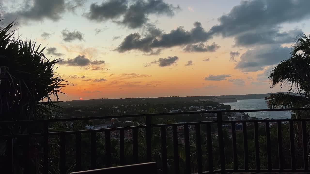 An incredible tropical golden and pink sunset from a high lookout of the famous tourist beach town of Pipa, Brazil in Rio Grande do Norte surrounded by green foliage during a warm summer evening