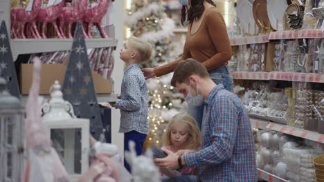 Vier-Leute-Im-Supermarkt.-Eine-Familie-In-Medizinischen-Masken-Im-Laden-Kauft-In-Zeitlupe-Weihnachtsdekorationen-Und-Geschenke.