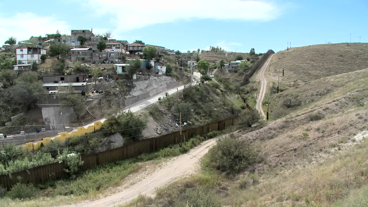 un animal corre por el camino frente a un pueblo en la ladera y los árboles soplan en el viento