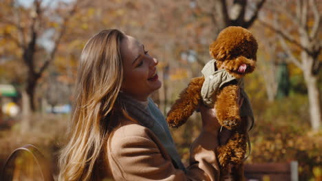 lovely young woman kissing toy poodle dog puppy holding doggy in hands at autumn park - slow motion portrait shot