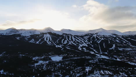 aerial cinematic drone view of breckenridge ski area and town from boreas pass late afternoon sunset over mountain tops mid winter upward motion