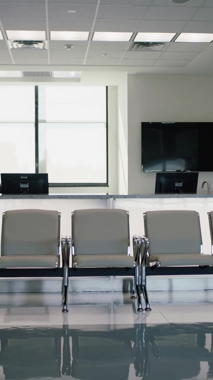 Video verticale: Telecamera in panoramica che mostra tre sedie grigie nella reception di un ufficio con due monitor.