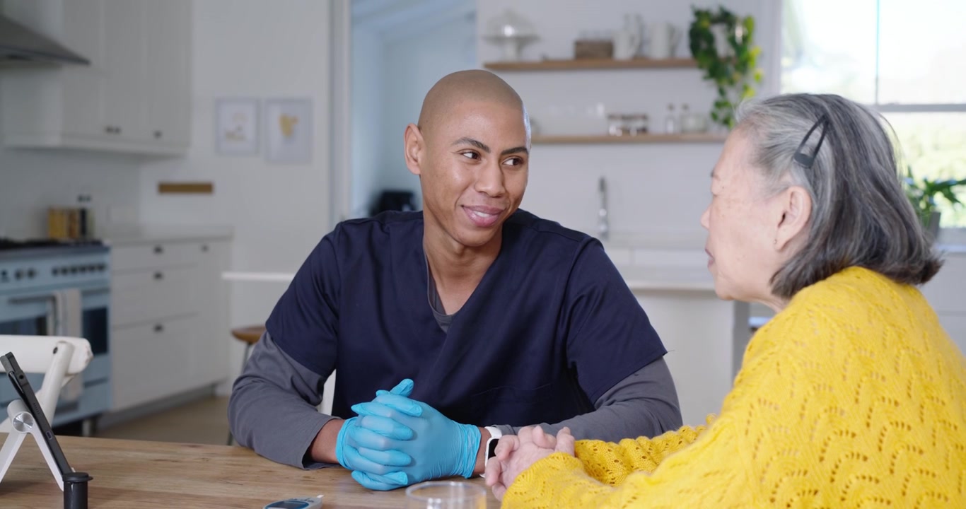 African American caregiver in scrubs seeing meter, showing sugar test to senior Chinese in kitchen