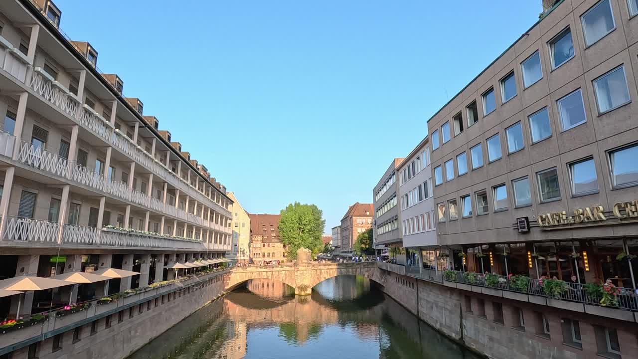 Daytime video pans along riverside architecture toward historic stone bridge in Nuremberg, Germany
