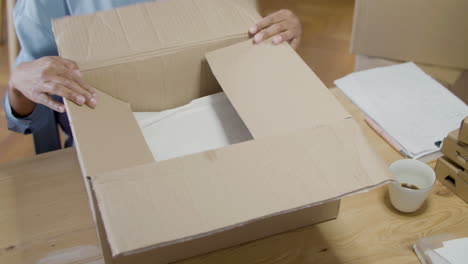 female office worker packing wrapped goods in cardboard parcel