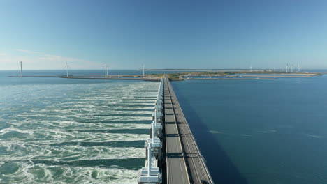 Vista-Aérea-De-La-Presa-De-La-Barrera-Contra-La-Marejada-Ciclónica-Del-Este-De-Scheldt-Con-Turbinas-Eólicas-En-El-Fondo-Cerca-De-Kamperland,-Zelanda