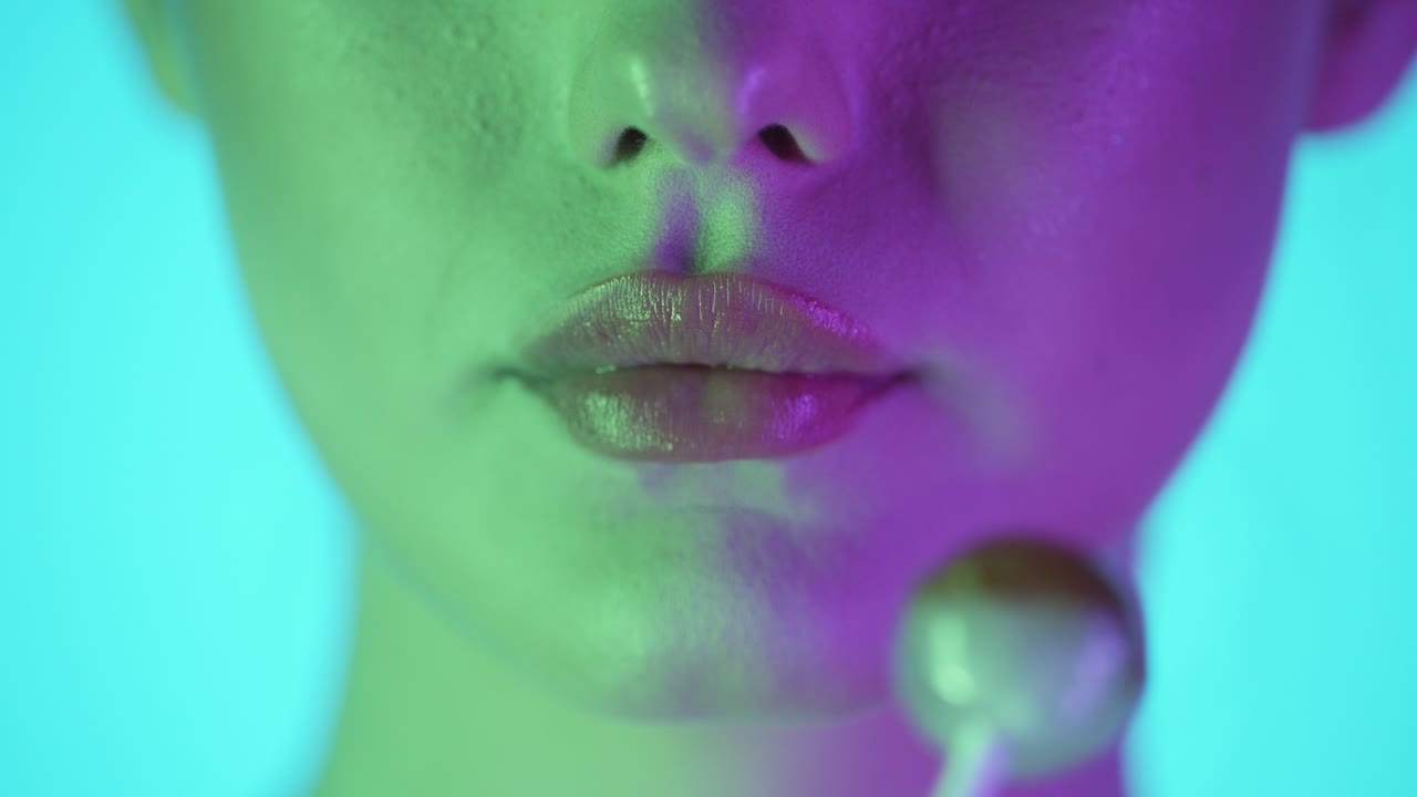 toma de cerca de los labios de una mujer joven lamiendo piruleta mientras se ve sexy y seductora en la cámara en cámara lenta contra un fondo turquesa en cámara lenta