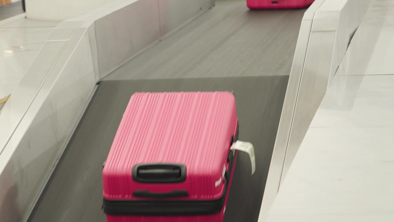 Una valigia rosa si muove sul nastro trasportatore del ritiro bagagli in un aeroporto. I viaggiatori aspettano nelle vicinanze per ritirare i loro bagagli. L'area è affollata di passeggeri in arrivo dai loro voli