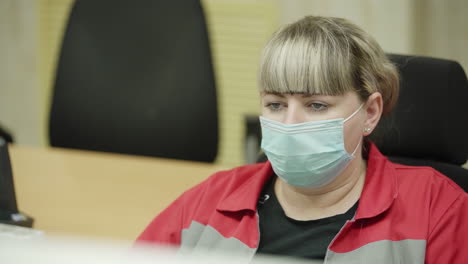 woman in a red uniform wearing a mask at a computer