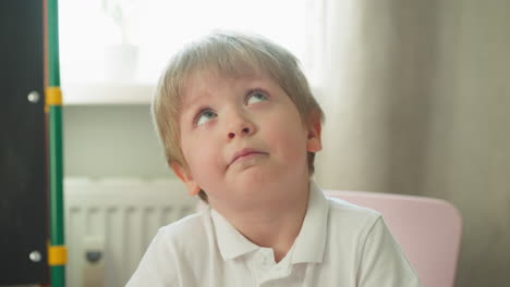 dreaming little boy looks up solving tasks at desk in class