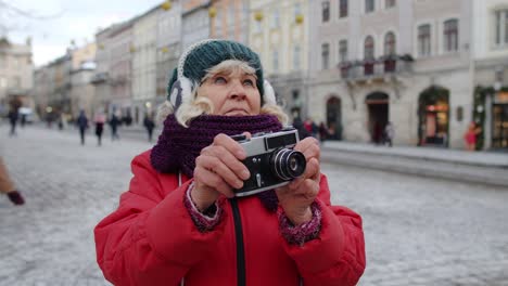 Senior-old-woman-tourist-taking-pictures-with-photo-camera,-using-retro-device-in-winter-city-center