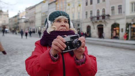 senior old woman tourist taking pictures with photo camera, using retro device in winter city center