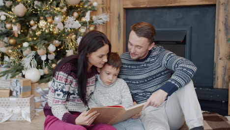 family reading a book by the christmas tree