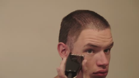 un joven guapo cortándose el pelo con una maquinilla de afeitar eléctrica - primer plano