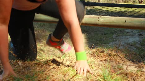 mujer decidida arrastrándose bajo la red durante una carrera de obstáculos