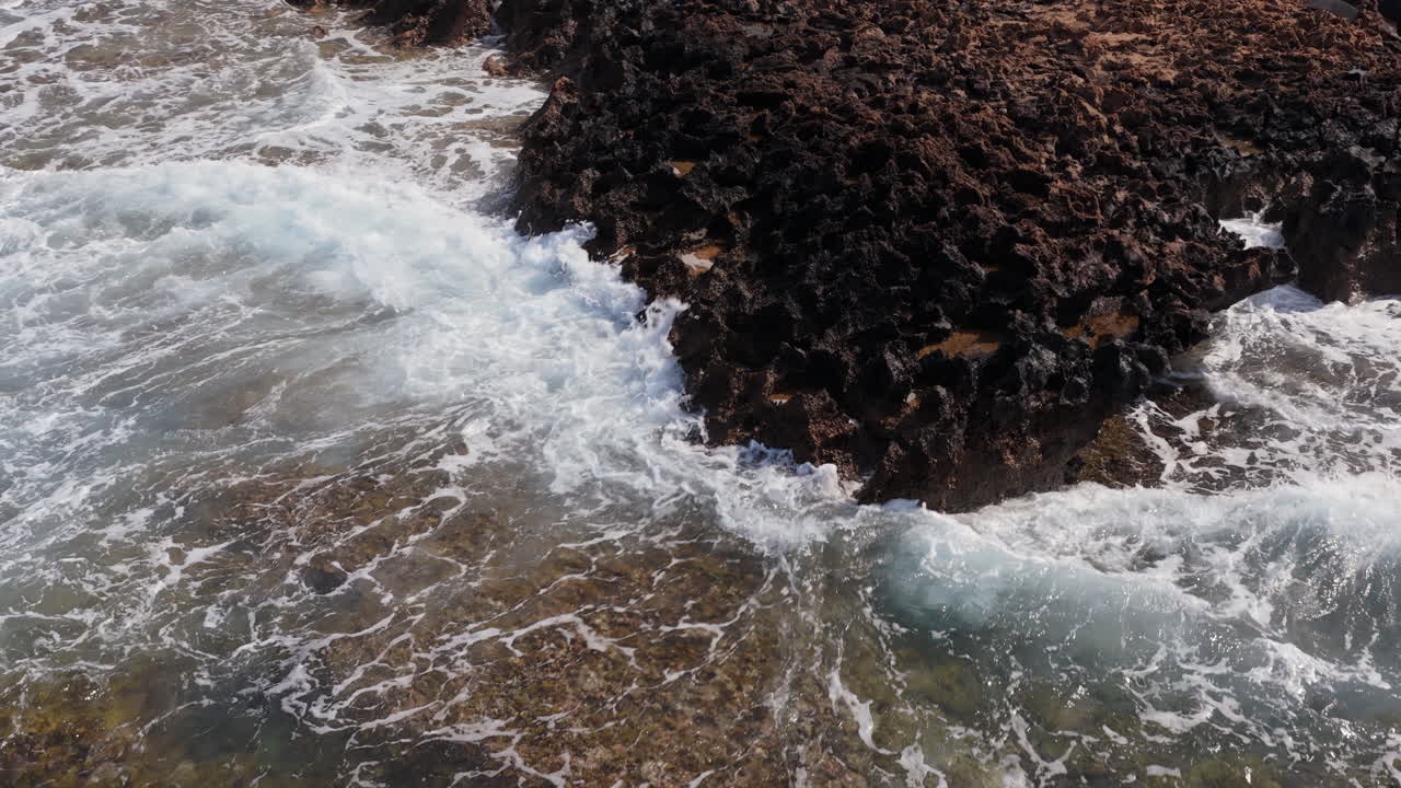 Ripresa aerea al rallentatore con drone di onde che si infrangono contro aspre rocce scure a Cipro.