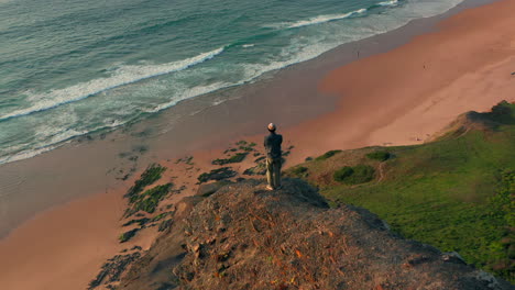 aerial: a man standing on a viewpoint watching the surfers in portugal