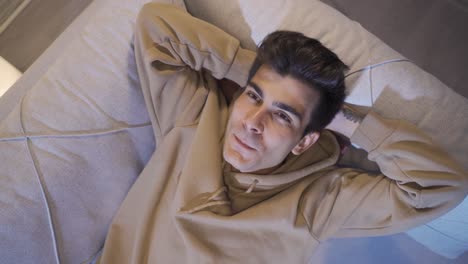 happy young man lying on sofa. thoughtful positive teenager.